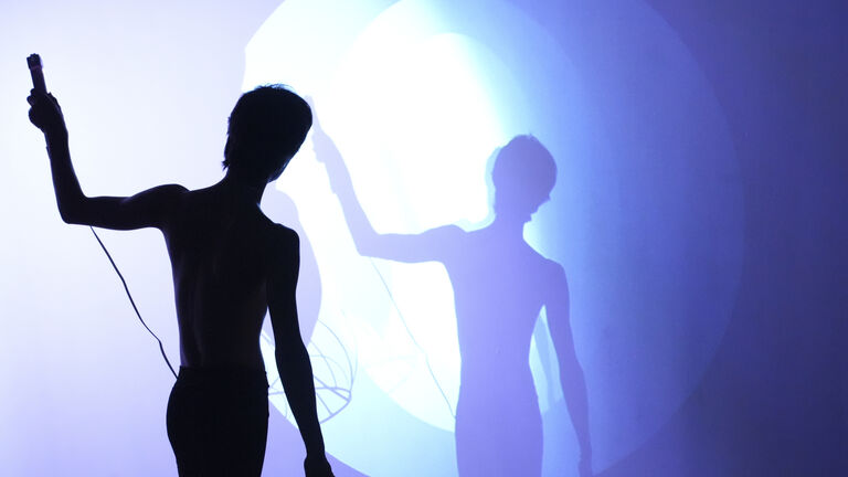 Hesam performing with a microphone. Lights and shadows bounce across the wall.