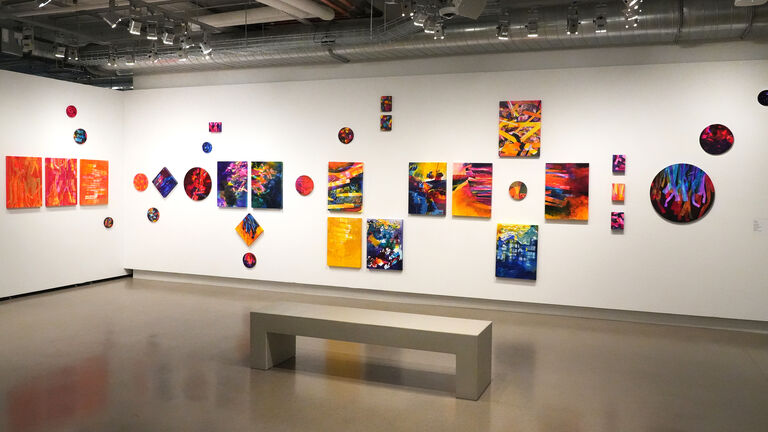 Colorful paintings hang on a white wall.