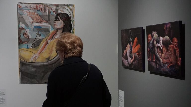  visitor with short blond hair stands with their back to the camera, looking closely at Scott Kuffner's large figurative painting Minerva Overlooking Venice. To the right on a darker wall, Kuffner's diptych Adam & Eve is also visible.