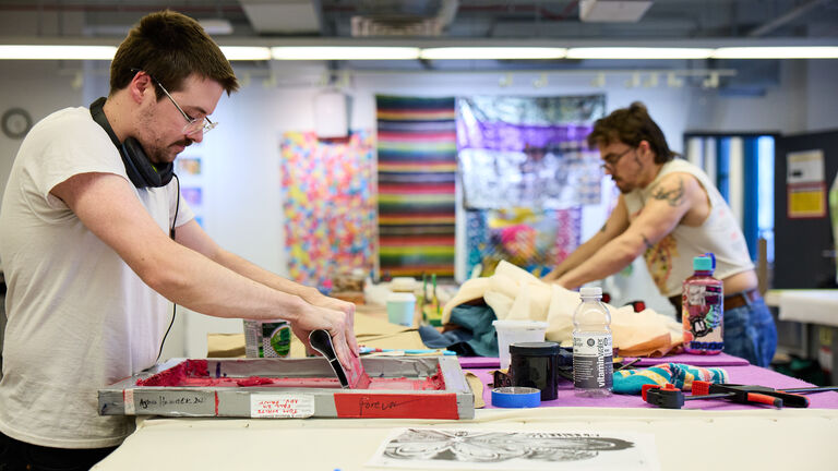 Two students screenprinting in a fibers classroom.