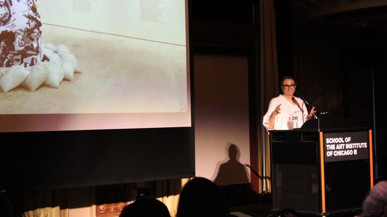 A person at a podium in front of a screen presenting.