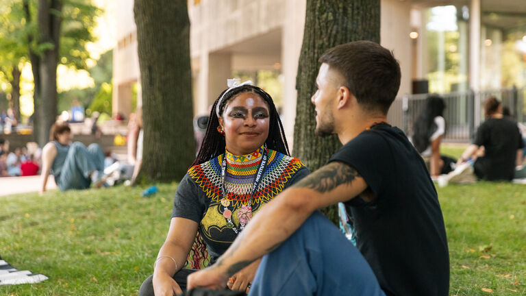 Students with varying skintones and gender identities sitting outdoors. 