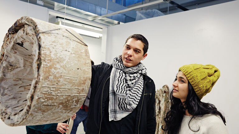 Two students view a hanging artwork in a gallery space. 