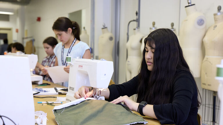 Middle school students of varying ethnicities, skintones, and genders, working with sewing machines. 