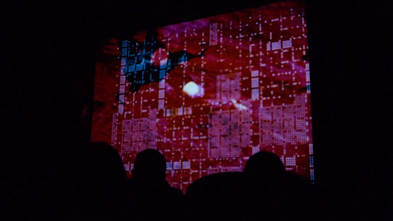 Projection of a red and blue abstract, pixelated artwork by Stan Vanderbeek. 
