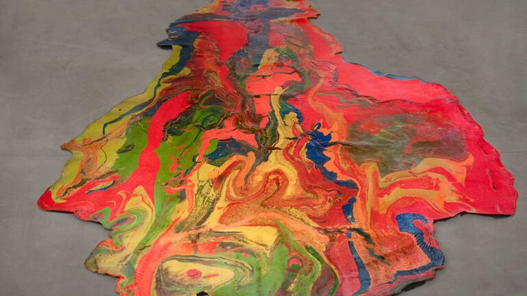 A flat, marbleized latex artwork poured directly on the floor. Colors of red, bright pink, green, blue, and yellow dominate.