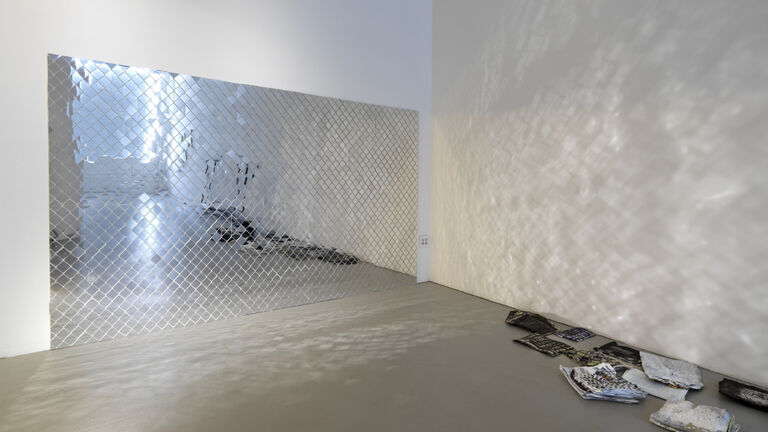 A gallery where a patterned mirror is reflecting light onto a collection of papers on the floor