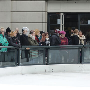 An image of a person amongst a crowd outside an ice skating rink, wearing a large transparent bubble on their head.