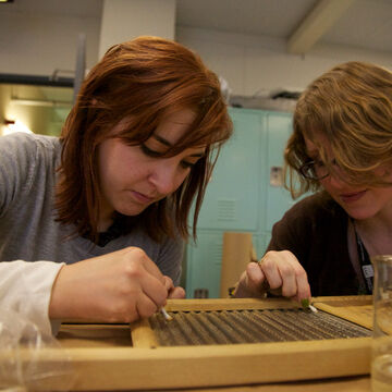 Two students clean an old washboard with cotton tips.