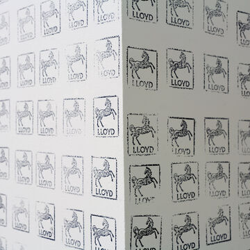 A close up image of a white wall with the stamps covering it in an even, close pattern. Each stamp has a horse and the words "LLOYD."