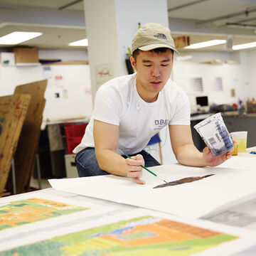 Student leaned over worktable and painting.