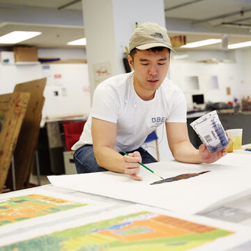 Student leaned over worktable and painting.