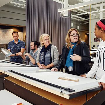 A group of people at a drafting table conversing. 