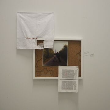 Documentation of a piece hung on a wall consisting of corkboard, a pinned page from a book, and some fabric as well as a photo of two people standing on a road in the middle.