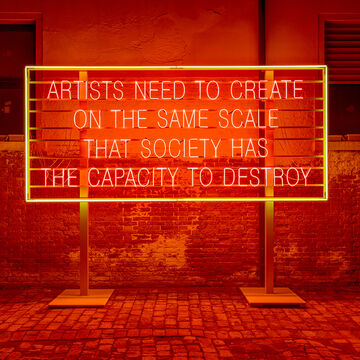 An imposing neon sign reads “ARTISTS NEED TO CREATE ON THE SAME SCALE THAT SOCIETY HAS THE CAPACITY TO DESTROY."