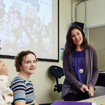 Professor is listening to a student share their perspective during a classroom discussion with images projected on a screen in the background.