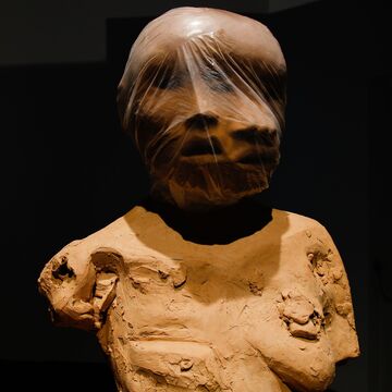 An artist’s piece depicting multiple faces covered by plastic, over a rough bust