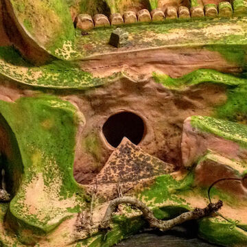 A green and tan closeup of a ceramics piece resembling rock formations mixed with manmade structures.
