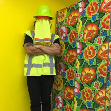 Image of an artist, face obscured, in high-vis gear against a floral backdrop