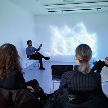 A professor sitting in a gallery with students observing a projection of a white and blue lights.