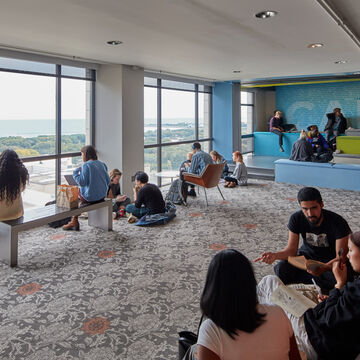 Students talking with each other and studying in a large lounge space on the fourteenth floor of an SAIC campus building overlooking Grant Park and Lake Michigan