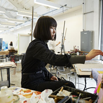 A person sitting at an easel painting in a studio.