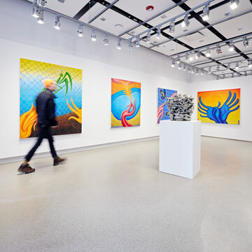 Patrons viewing paintings with saturated yellows, blues, and pinks within large gallery space.