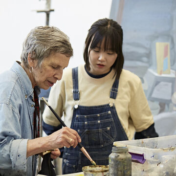 A professor cleaning a paintbrush with a student watching carefully. 