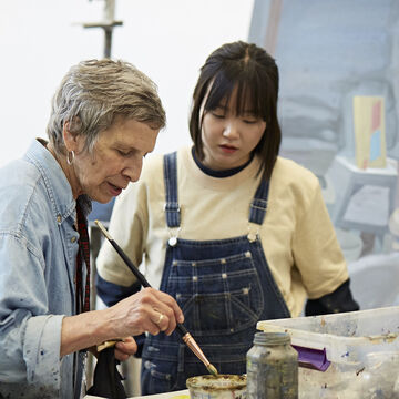 A professor cleaning a paintbrush with a student watching carefully.