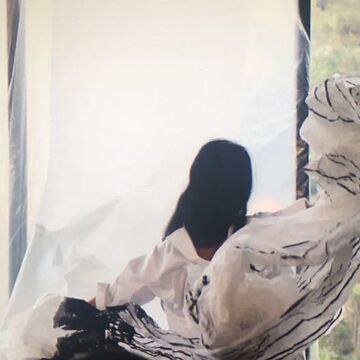 Video still of a person in a gallery observing a paper mache object