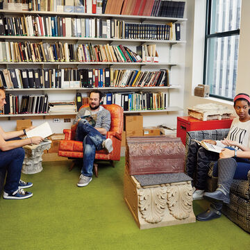 Four people sit in a louge surrounded by books. 