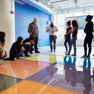 An image of some students observing a large piece of art on the floor in the School of the Art Institute of Chicago's gallery space.