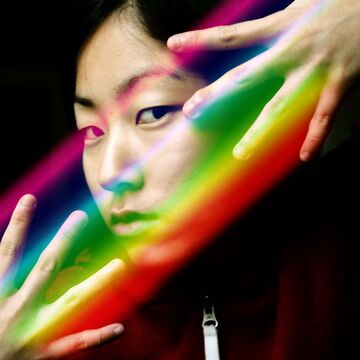 An image of Noel King with her hands and fingers over her eyes with a rainbow. 