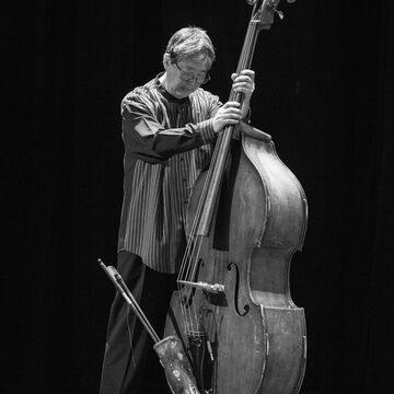 A black and white photo of Tatsu Aoki holding a double bass instrument.