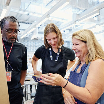 A student shows two teachers an image on her phone in an art classroom