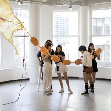 A group of students interacting with a large hanging piece of art.
