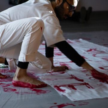 Person in a white jumpsuit writes over a tarp in red paint