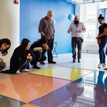 Arts Admin students listening to instructor in gallery space while looking at large, brightly colored tiles on floor.