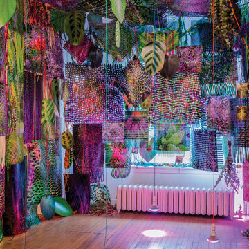 Various colorful prints, leaves and lights hanging from the ceiling of a gallery space.