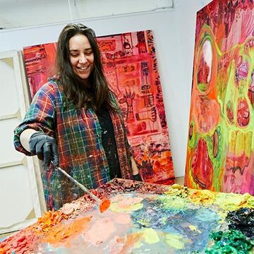 A student using a paint brush to create a colorful picture on canvas.