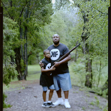 Portrait of a middle aged man and a young boy, both holding a rifle.