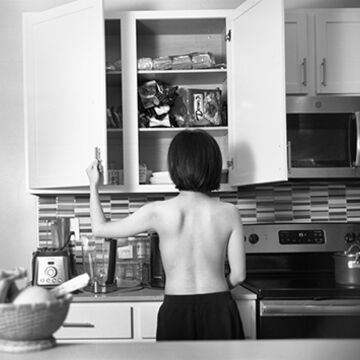 A topless person rifling through kitchen cabinets