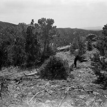 Black and white image of a blurred person running across a landscape