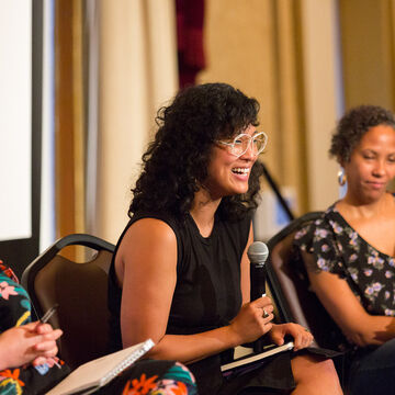 Three people sitting on a stage speaking to a room of people. 