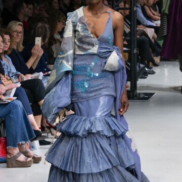 Model walking down runway in purple, ruffled gown.