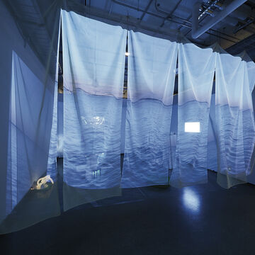 Multiple large, transparent sheets with a projection of water hanging in a gallery space. 