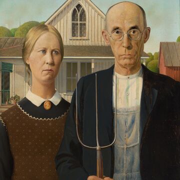 Two farmers, a husband and white, pose with a pitchfork in front of a farmhouse
