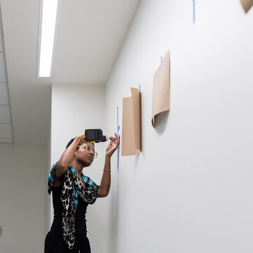 A student using a power tool to secure a piece of art to the wall. 