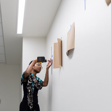 A student using a power tool to secure a piece of art to the wall.