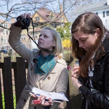Two students outdoors. One is taking a photo of something out of frame with a camera. 